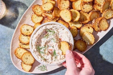 A hand dipping an everything bagel chip into Salmon Cream Cheese dip. - select to zoom