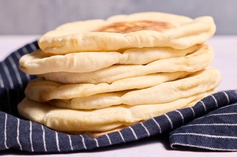Stack of Sourdough Pita Bread on a dark blue napkin with stripes, photographed from the side. - select to zoom