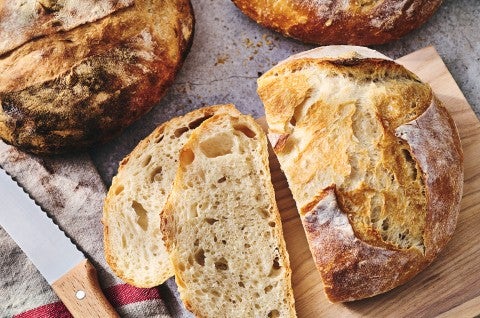 Fresh baked loaves of No-Knead Crusty White Bread on a table with jam and butter and slices on a cutting board. - select to zoom