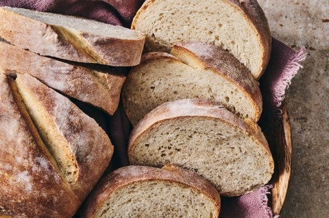 A rustic loaf of white bread in a basket with several slices. - select to zoom