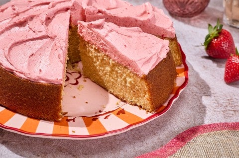Brown Sugar Strawberry Frosted Cake seen from the side showing a thick layer of frosting and a golden cakey interior.