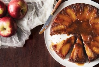 A freshly baked Apple Upside-Down Cake, inverted onto a serving platter with a slice removed.
