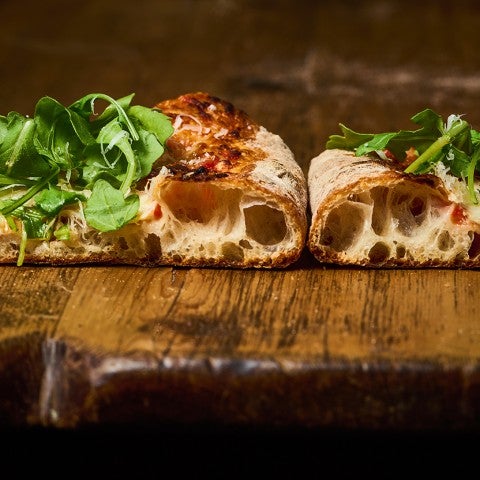 Two slices of artisanal pizza shown from the side with large air pockets in the cooked dough. - select to zoom