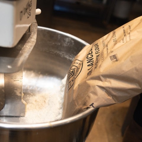 Flour being poured into a stand mixer bowl in preparation of making dough. - select to zoom